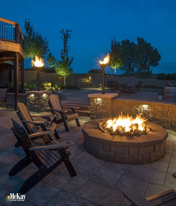Ilumine um poço de fogueira ao ar livre com as luzes da parede do assento. Veja mais ideias populares de iluminação de fossos de incêndio. | McKay Landscape Lighting - Omaha Nebraska