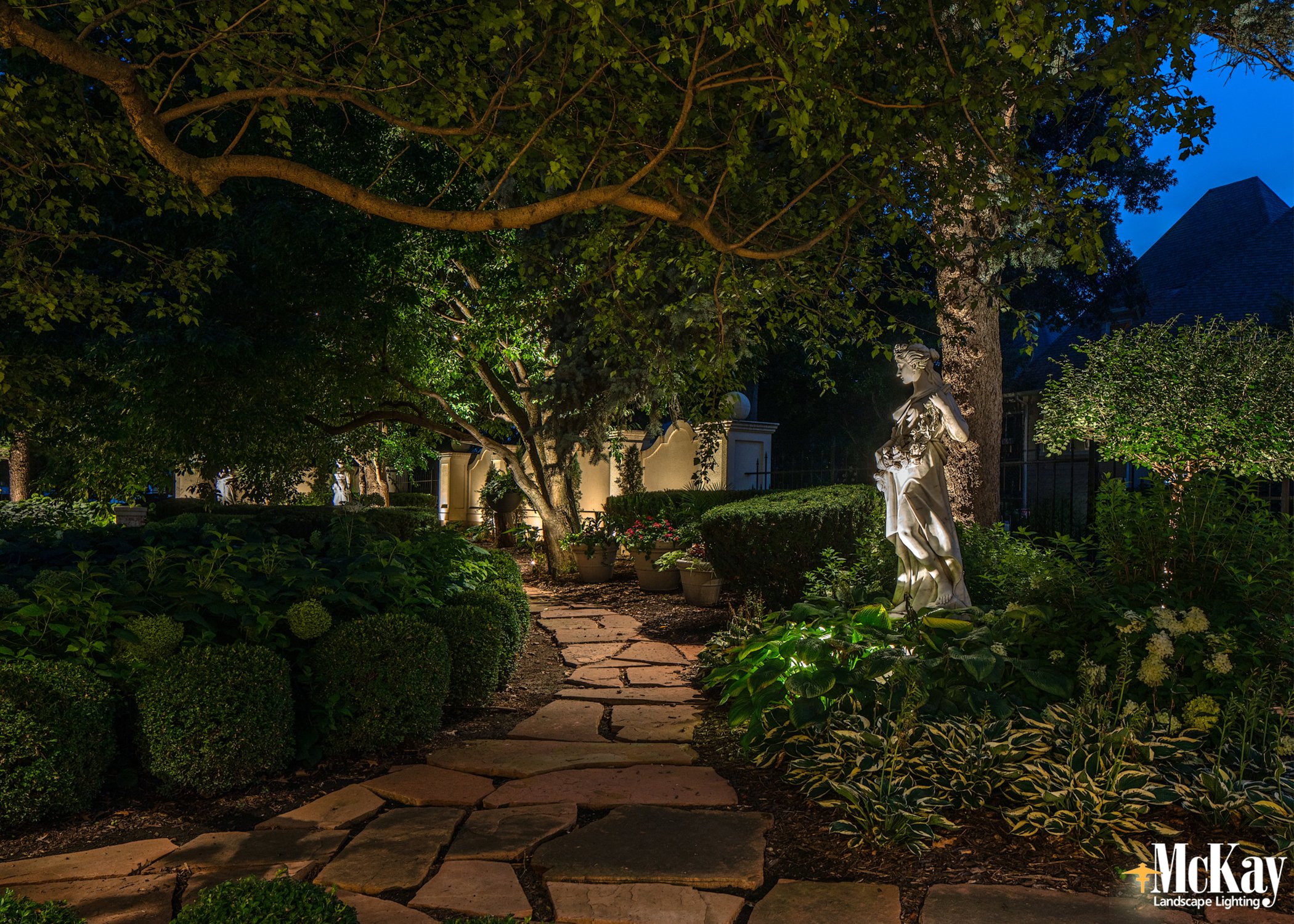 Garden statue and pathway illuminated by custom landscape lighting at a luxury Omaha residence.